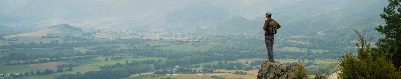 A man standing on the top of a cliff looking down at a city