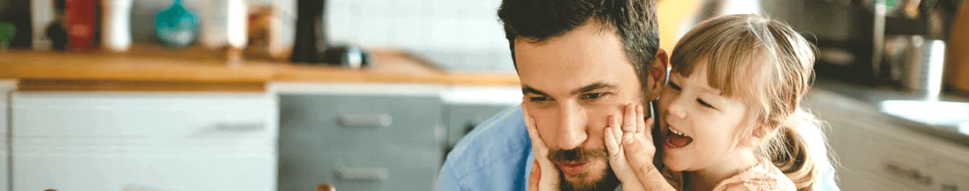 A young girl smiling and holding a man's face with her hands