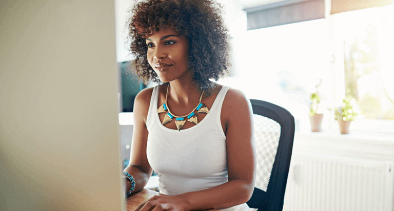 A woman sits in an office chair while she smiles at her computer screen