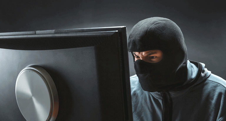 A man in a ski mask angrily looking at a large computer screen