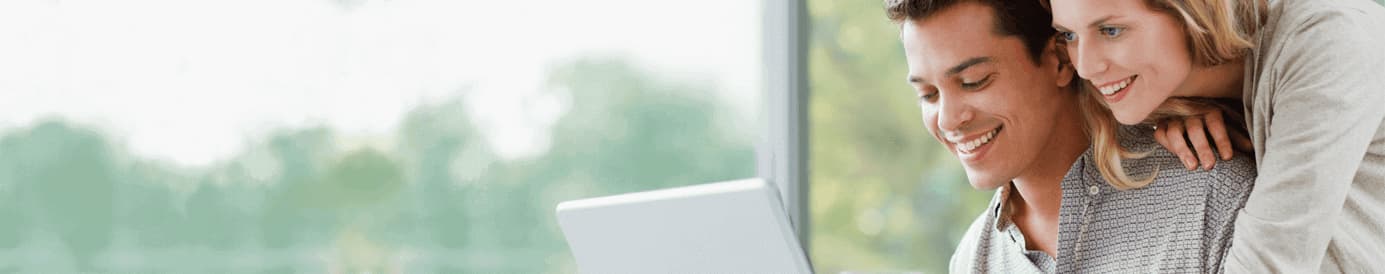 A smiling woman leaning on a man who is smiling while looking at his laptop and holding a credit card with his left hand