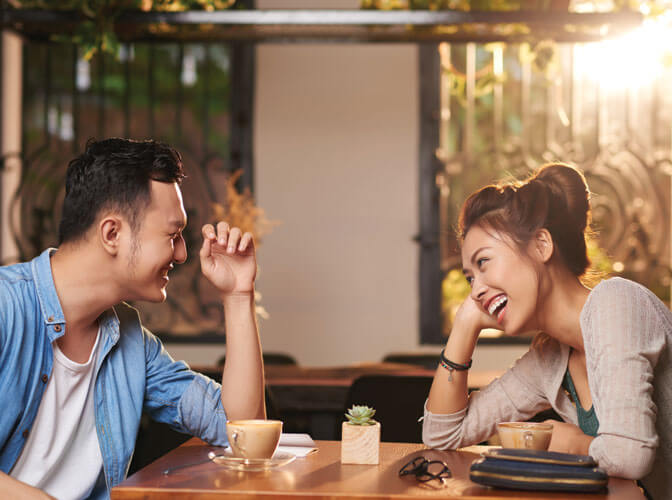 Man and woman sitting at a table in a restaurant having coffee and laughing together