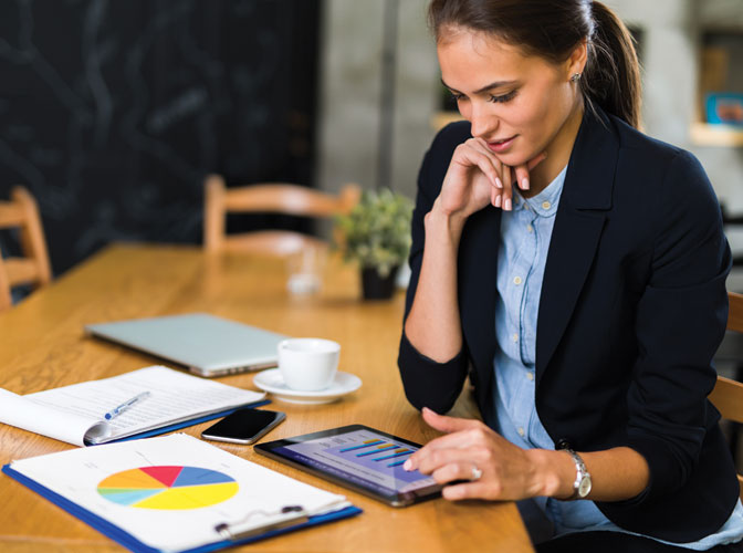 woman sitting at a table looking at a pie chart and her ipad