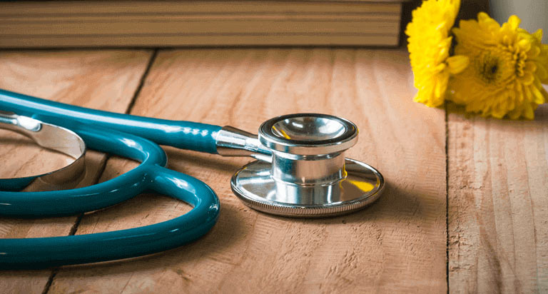 A blue and silver stethoscope with yellow flowers in the background