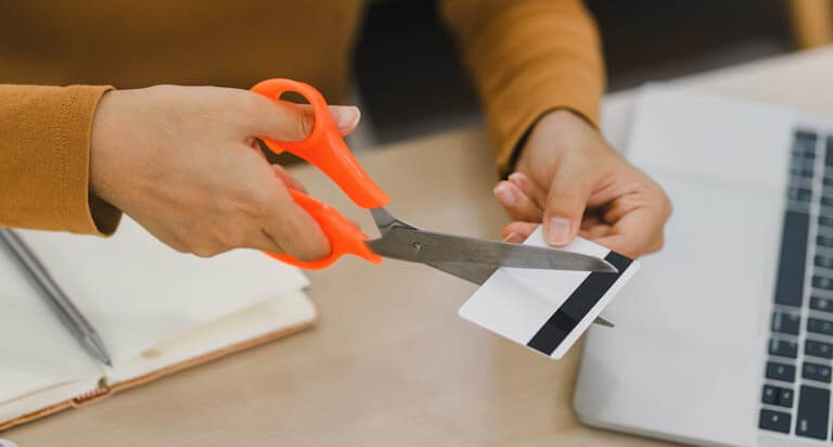 A woman's hands positioned over a desk as she cuts the credit card in her hand with scissors.