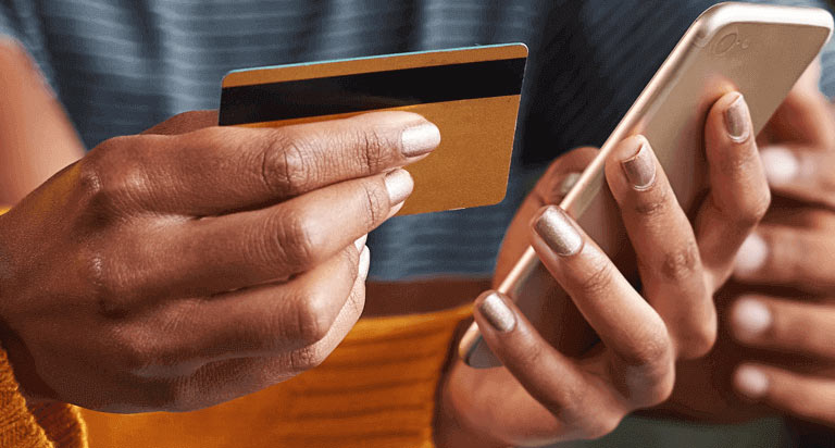 A woman holding a cellphone in her left hand and a credit card in her right hand