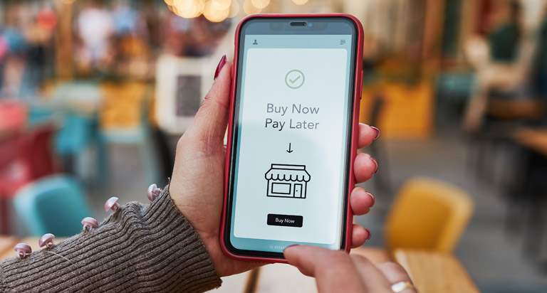 Hands hold a mobile phone. The phone’s screen shows a shop icon with the text 