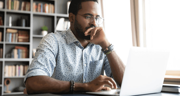 A man wearing glasses looking down at his laptop