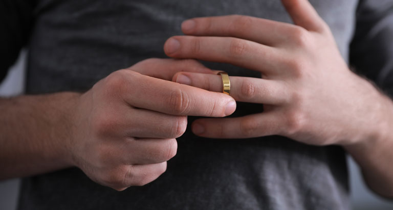 Mid-body crop of a man in a gray t-shirt removing his wedding ring.