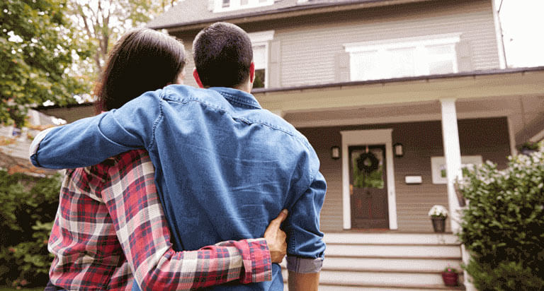 A man and a woman hold each other in front of a house