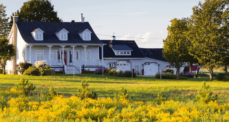 A large white farmhouse with a large three car garage and a white detatched shed behind it