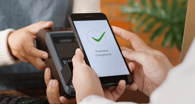 A person holding a phone to a payment terminal while the screen read Payment Completed with a green checkmark