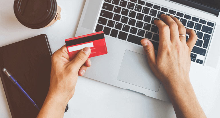 A person holding a credit card in their left hand while typing on their laptop with their right hand