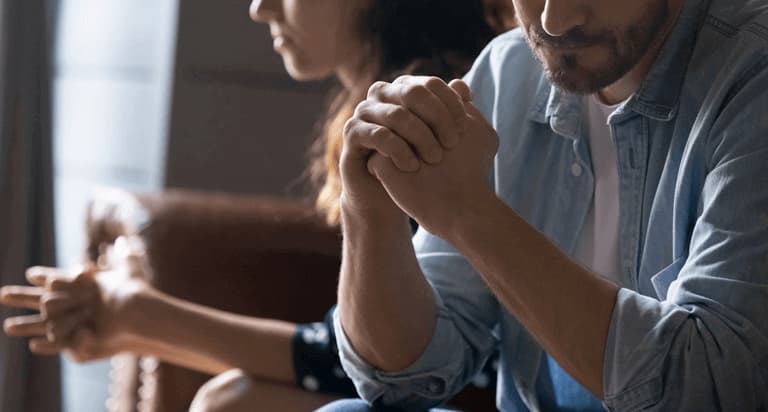 A man and a woman sit next to each other clasping their hands