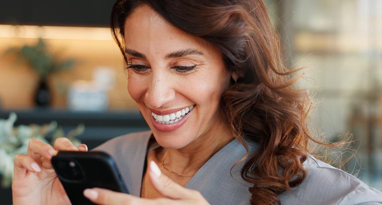 A business woman with dark red hair smiles brightly as she looks down at her phone and scrolls.