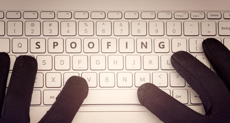 Two hands in black gloves sit on a keyboard with the word 'spoofing' centered on the third row of keys.