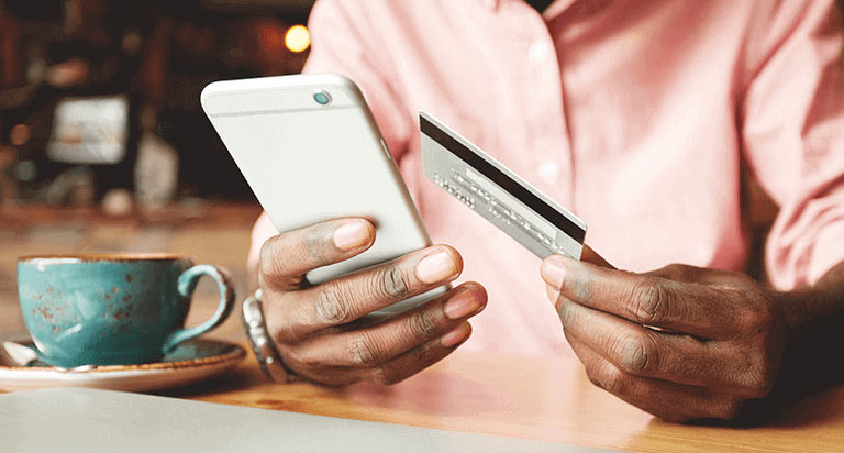 A man holding a cellphone in his right hand and a credit card in his left hand