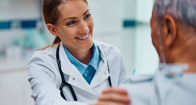 A doctor puts her hand on a patient’s shoulder as she speaks to him in a doctor’s office.