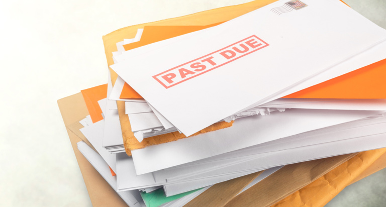 A stack of mail sits on a surface, some opened. On the top is a white envelope with the words “Past Due” stamped in red.