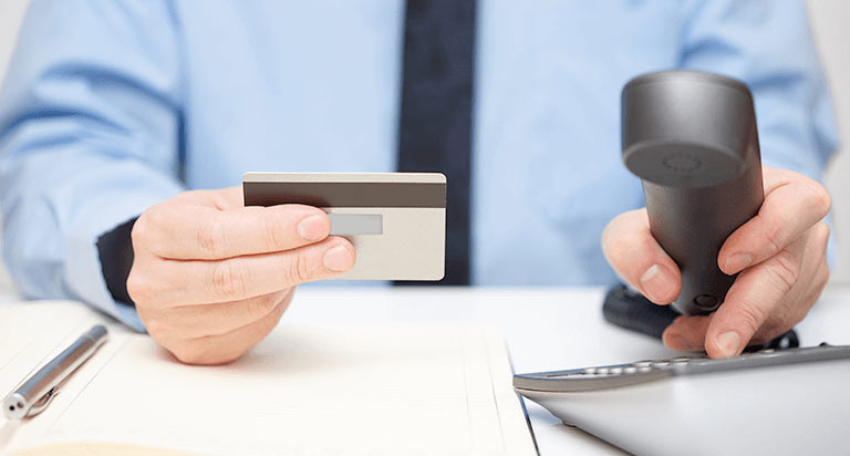 A man holding a credit card with his right hand while holding a phone receiver and dialing a number with his left hand