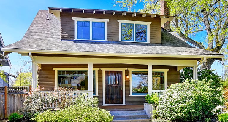 The front of a small modern house. The house has a brown exterior with a brown front door, and large first and second floor windows.