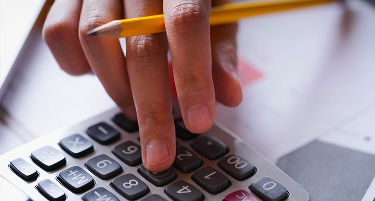 A person holding a pencil while typing into a calculator