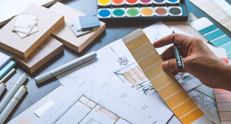 A desk with home improvement architectural designs and someone holding a pen looking over the plans.