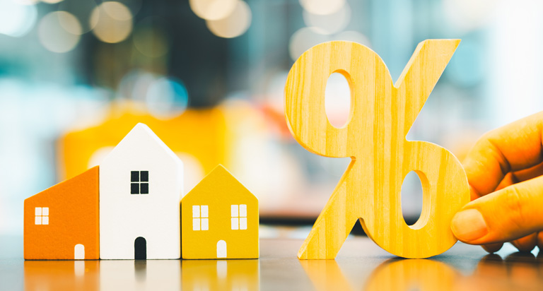 A smooth surface with three wooden block houses lined up in a row. A larger percentage sign made of wood sits next to them.