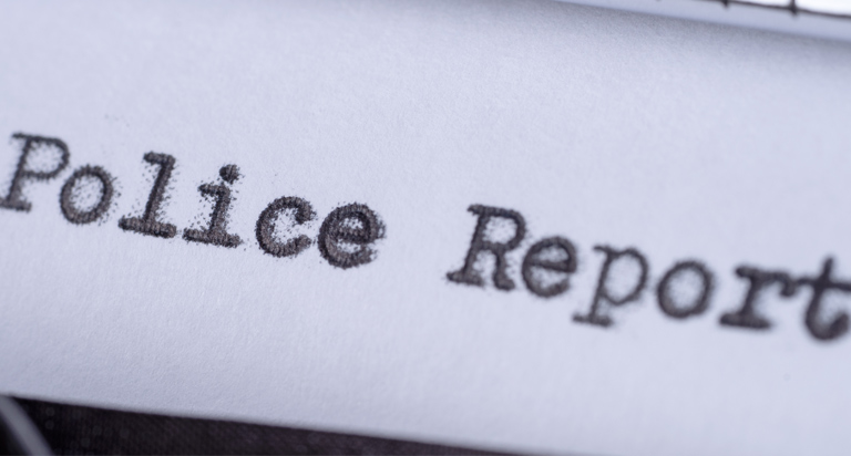 Close-up view of a vintage typewriter with the words “police report” typed out on the page in black ink.
