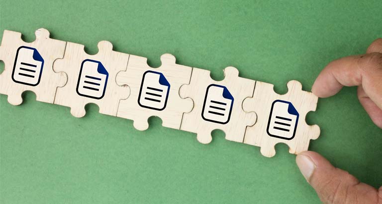 A hand links puzzle pieces together in a row on a green surface. Each puzzle piece has the image of a file icon printed on it.