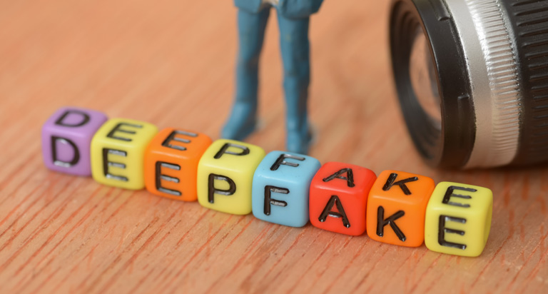 Small, lettered blocks of different colors are lined up on a wooden surface to spell the word 'DEEPFAKE'.