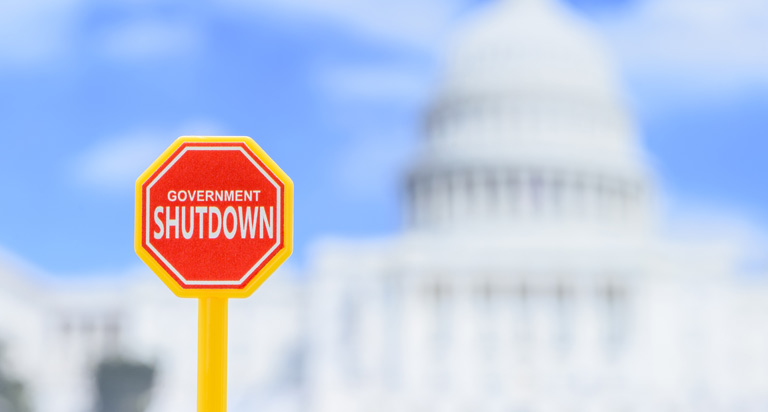 A blurred U.S. capitol building in the background with a red sign in the foreground that says 