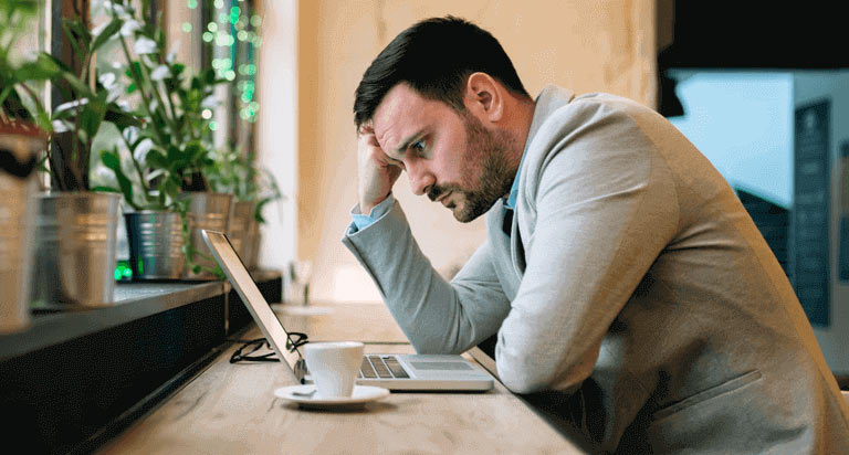 A man looking down at his laptop with an unhappy expression
