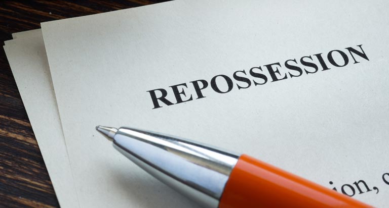 A document rests on a wood surface with the title 'REPOSSESSION'. The tip of a ballpoint pen is visible next to the copy.