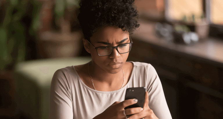A woman wearing glasses stares intently at her cellphone screen