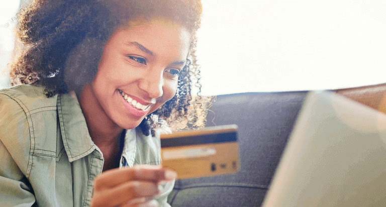 A woman holding a credit card in her right hand while looking at her laptop and smiling