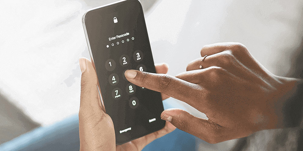 A person holds a cellphone with their left hand while their right hand enters a six-digit passcode on the phone screen