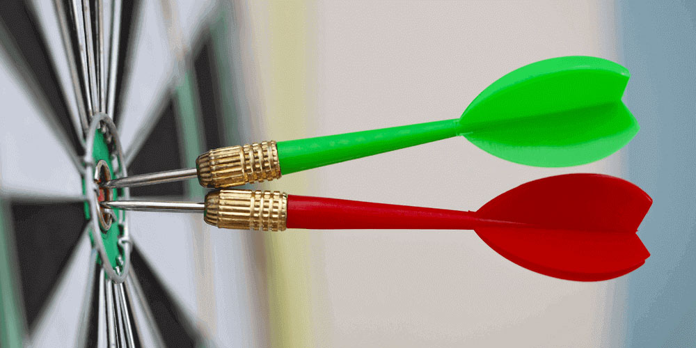 A green dart and a red dart in the center of a bullseye