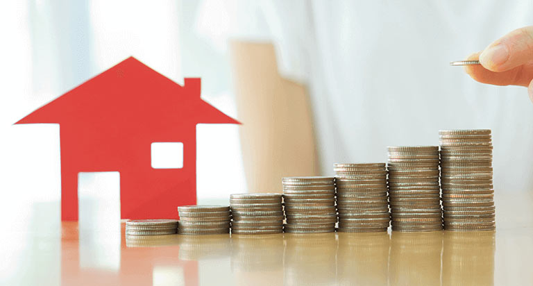 A person stacking coins into a step formation in front of a cutout of a little red house