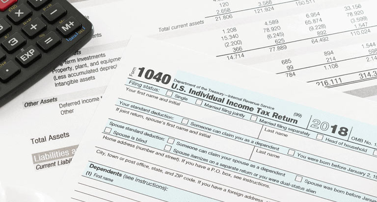 A US Individual Income Tax Return Form resting on other papers and a calculator