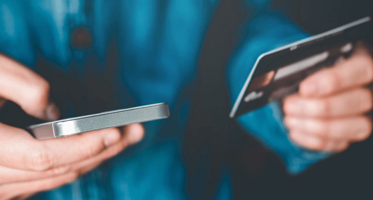 A person in a blue button down is holding their phone in one hand and their credit card in the other.