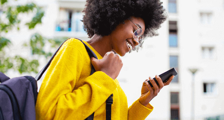 A woman wearing glasses and a backpack looking at a cellphone she is holding in her left hand