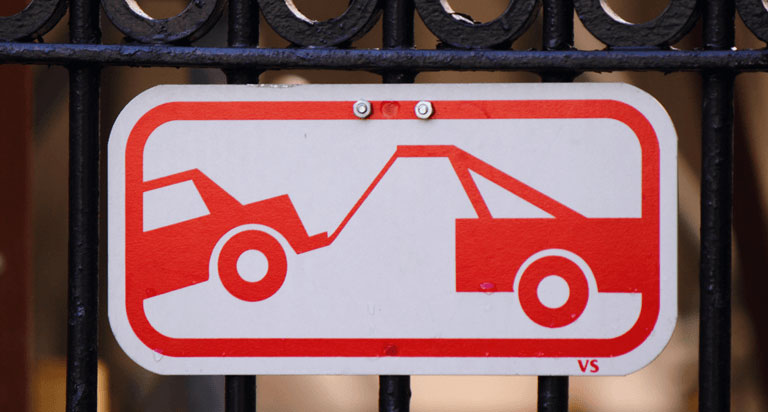 A red and white tow sign attached to an iron fence.