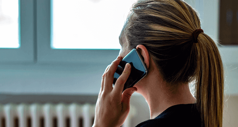 A woman is talking on her cell phone inside of her house. She is holding the smartphone to her ear.