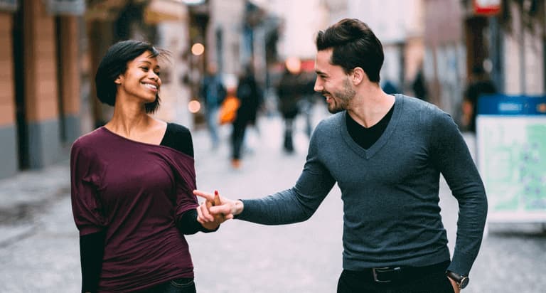 A woman and a man walking down the street while holding hands and smiling at each other