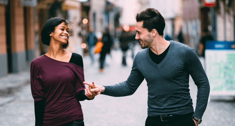 A man and woman are walking down a brick city street while holding hands.