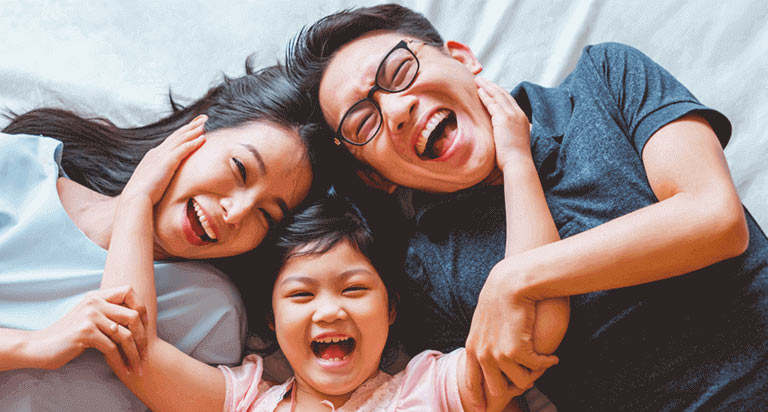 A smiling woman and a smiling man with glasses being hugged by a young child