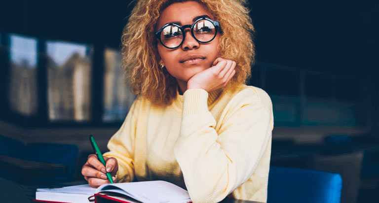 A woman with glasses looks up while writing in a book