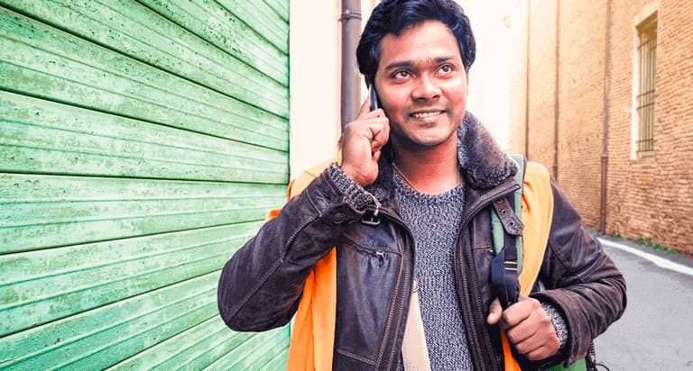 A man smiling while holding a cellphone to his right ear