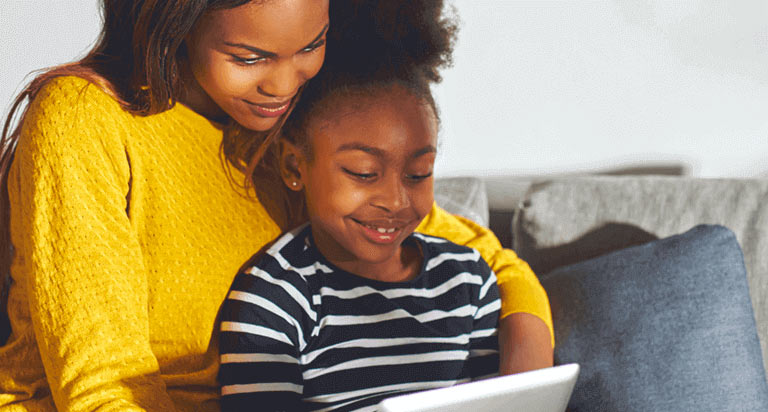 A woman and a young girl looking down and smiling at a tablet